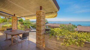 A covered patio with a stone pillar, a wooden table, and chairs. - Marina Loft (Moniga del Garda)