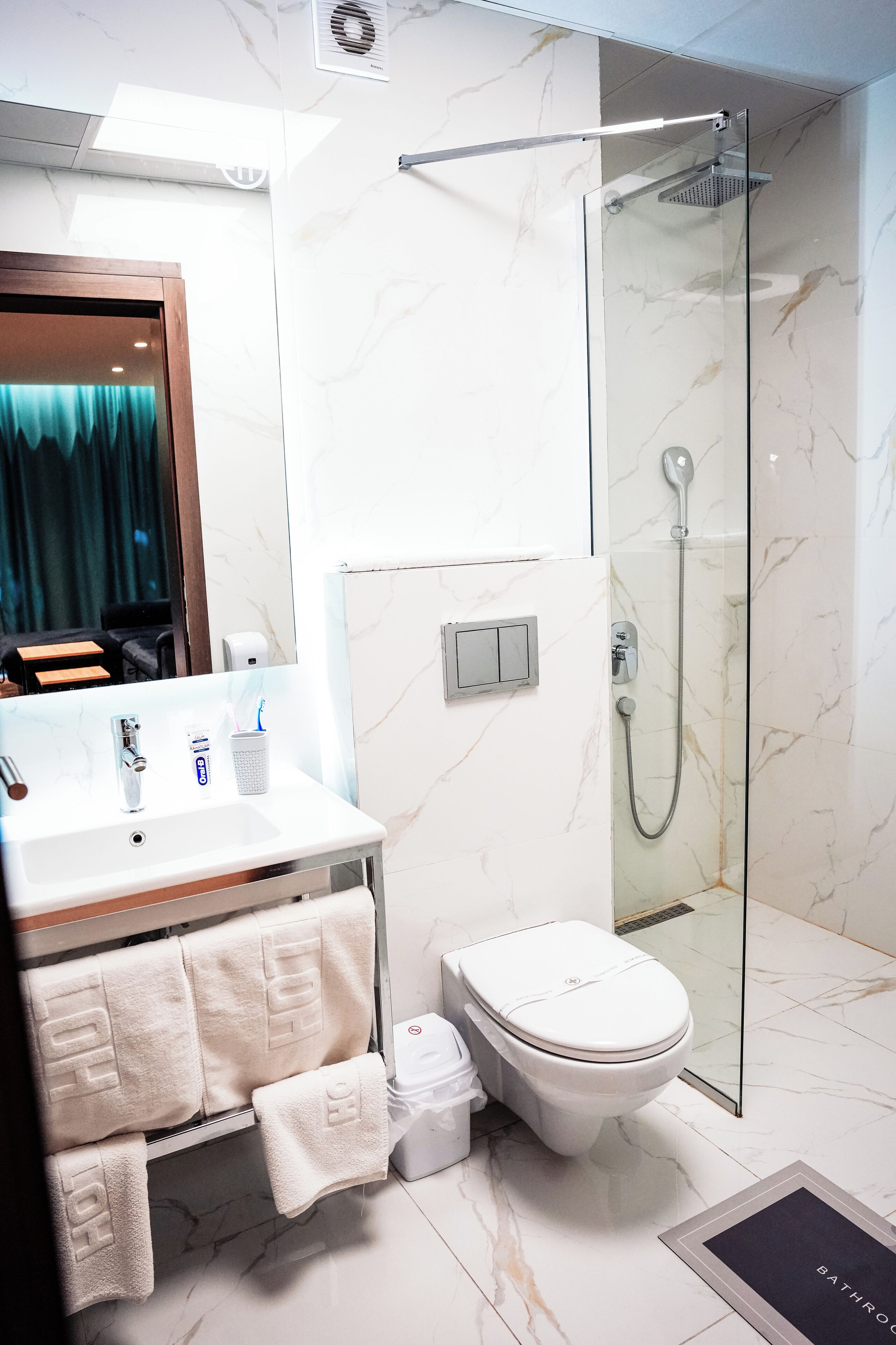 Un baño moderno con cabina de ducha de vidrio, un lavabo blanco con espejo y un inodoro.
