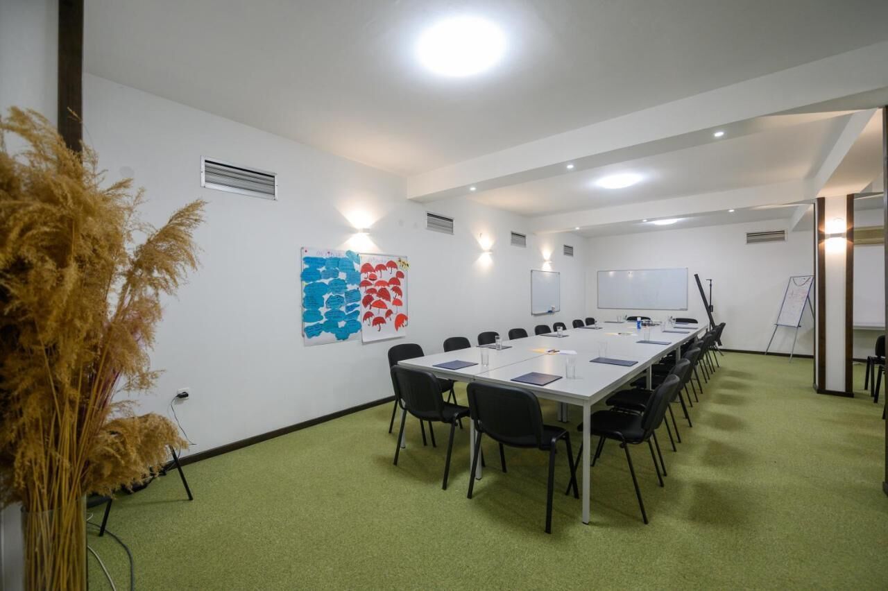 Un salón de conferencias con una larga mesa, sillas negras, una pizarra y una pantalla de proyector.