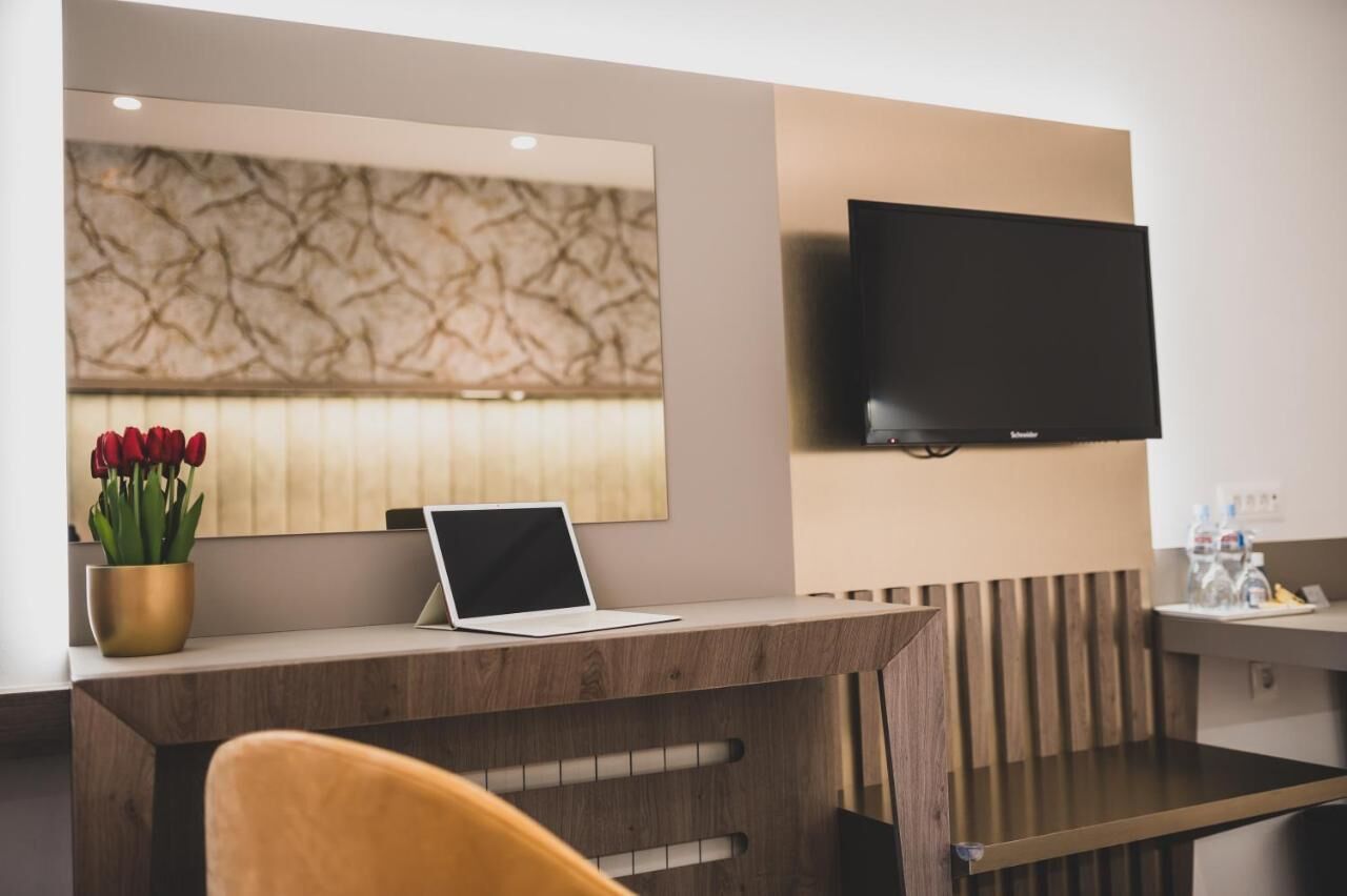 Zona de recepción de hotel con un mostrador de madera, una computadora portátil, un televisor de pantalla plana y un jarrón de tulipanes rojos.