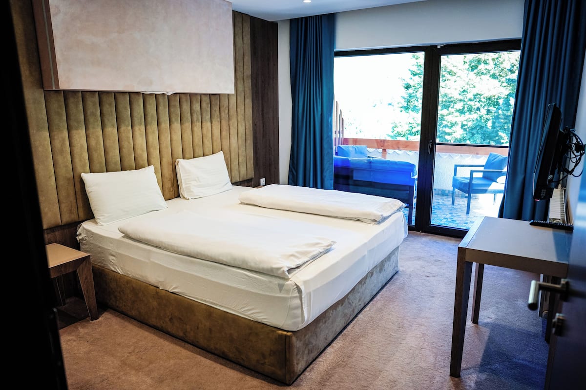 Una cama doble con cabecera de madera, una mesita de noche y vistas a un espacio exterior con una silla azul.