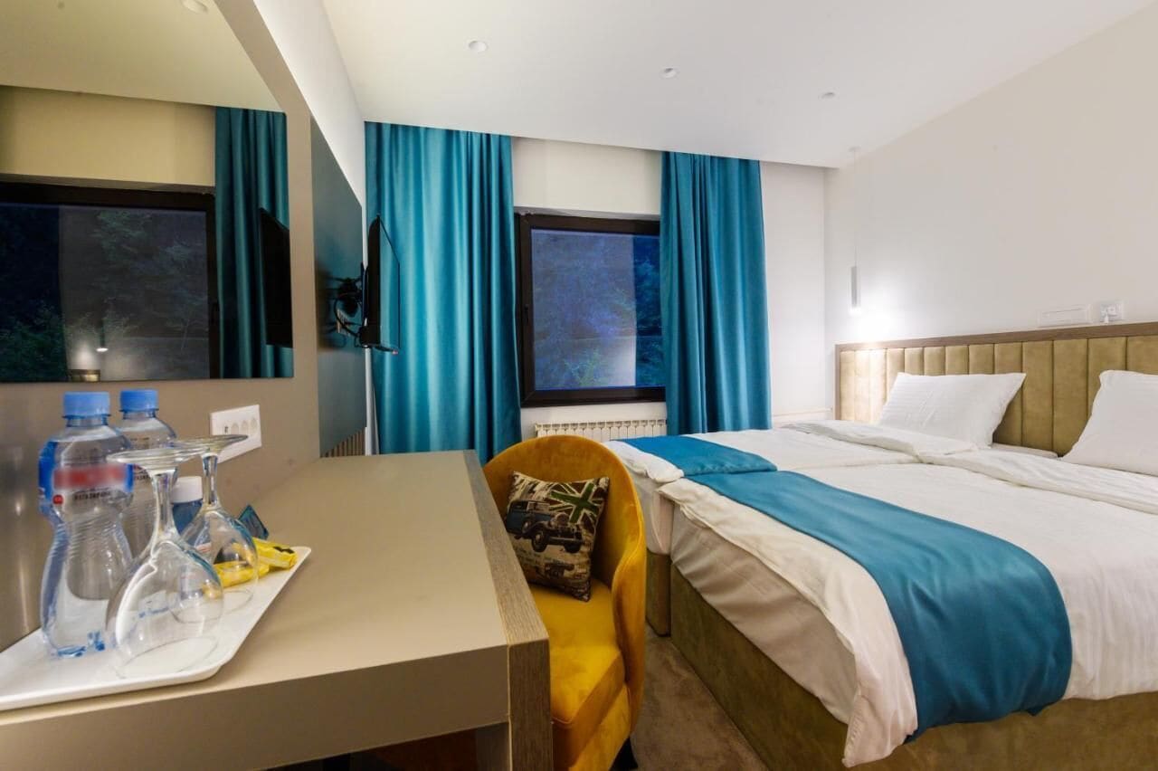 Ett hotellrum med en säng, ett skrivbord med vattenflaskor och glas, och en stol.
