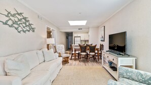 A modern living room with a sofa, dining table, chairs, and a TV. - Recently Renovated, ocean view condo + Free Attraction Tickets! (Myrtle Beach)