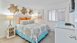 A bedroom with a bed, bedside tables, a TV, and a window with blinds. - Recently Renovated, ocean view condo + Free Attraction Tickets! (Myrtle Beach)