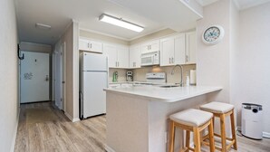 A modern kitchen with white cabinets, a built-in microwave, and a large island with bar stools. - Recently Renovated, ocean view condo + Free Attraction Tickets! (Myrtle Beach)