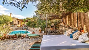 Un espace extérieur dallé de pierres, avec une piscine, un coin salon abrité et un lit agrémenté de coussins.