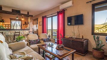 Een gezellige woonkamer met een bank, stoelen, een salontafel en een televisie. Er is een balkon met rode gordijnen en uitzicht op de woestijn.