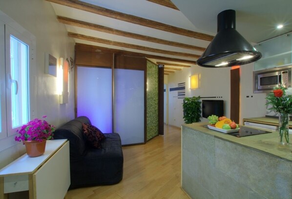 A modern kitchen with a central island, wooden beams on the ceiling, and a black pendant light.