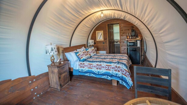 Una habitación tipo tienda de campaña, acogedora y circular, con cama de madera, un pequeño escritorio y una silla.
