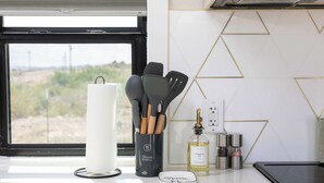 A kitchen counter with a window, a white towel dispenser, a utensil holder, a bottle of canola oil, and a spice rack. - Container Home @ Stardust Big Bend 5 min from Park (Terlingua)