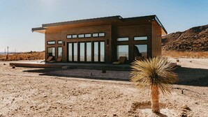 A modern building with large windows, a flat roof, and a desert landscape. - Container Home @ Stardust Big Bend 5 min from Park (Terlingua)