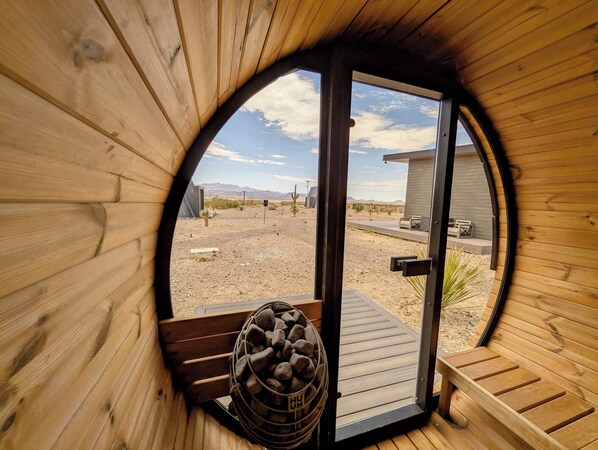 Une pièce circulaire en bois, avec une porte donnant sur un espace extérieur doté d’une terrasse en bois et d’un panier en métal rempli de bois de chauffage.