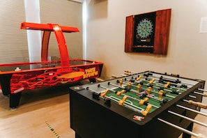 Twee tafelvoetbaltafels, waarvan één met een rode omlijsting en de andere met een zwarte, in een ruimte met een dartbord aan de muur.