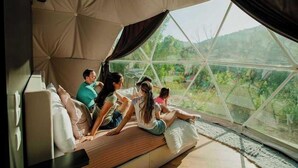 Une famille se trouve dans une pièce qui ressemble à une tente, avec vue sur la verdure environnante.