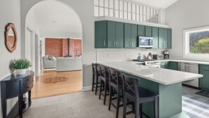 A modern kitchen with green cabinets, a white island, and a view of a brick wall and living area. - Home in Stowe with beautiful view of mountains

 (Stowe)