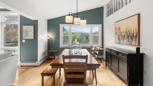 A modern kitchen with a dining table, chairs, pendant lights, and a large window with a view of trees. - Home in Stowe with beautiful view of mountains

 (Stowe)