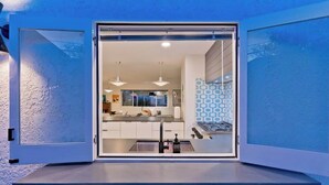 A modern kitchen with white cabinets, a stainless steel countertop, and pendant lighting. - Navigate Stays Iconic Home w/ Salt Pool Spa Casita (Palm Springs)