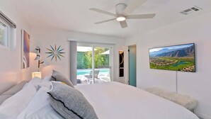A bedroom with a large bed, a ceiling fan, a painting, and a view of a pool and mountains. - Navigate Stays Iconic Home w/ Salt Pool Spa Casita (Palm Springs)