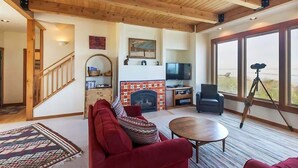 Ein gemütliches Wohnzimmer mit Kamin, Fernseher und einem großen Fenster mit Blick auf eine reizvolle Landschaft.
