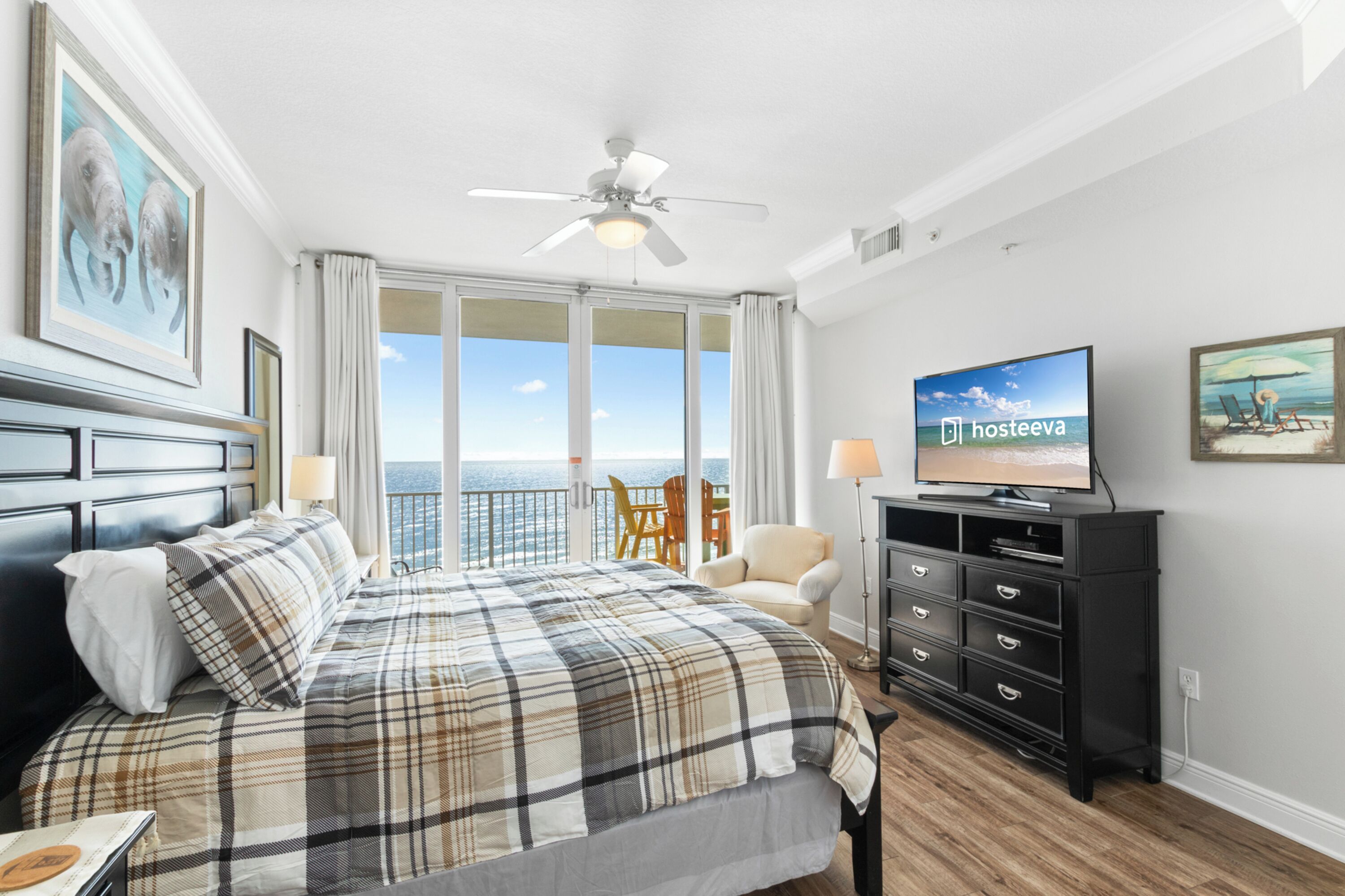 A hotel room with a large bed, a television, a ceiling fan, and a balcony with a view of the sea.
