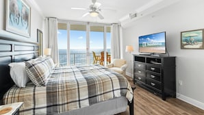 Ein Hotelzimmer mit einem großen Bett, einem Fernseher, einem Deckenventilator und einem Balkon mit Meerblick.