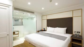 A modern hotel room with a large bed, a bedside table, a nightstand, a glass shower enclosure, and a white door.