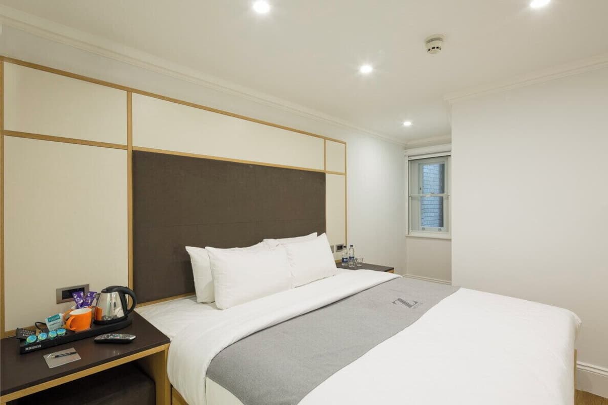 A hotel room with a large bed, a bedside table with a kettle, a cup, and a remote control.