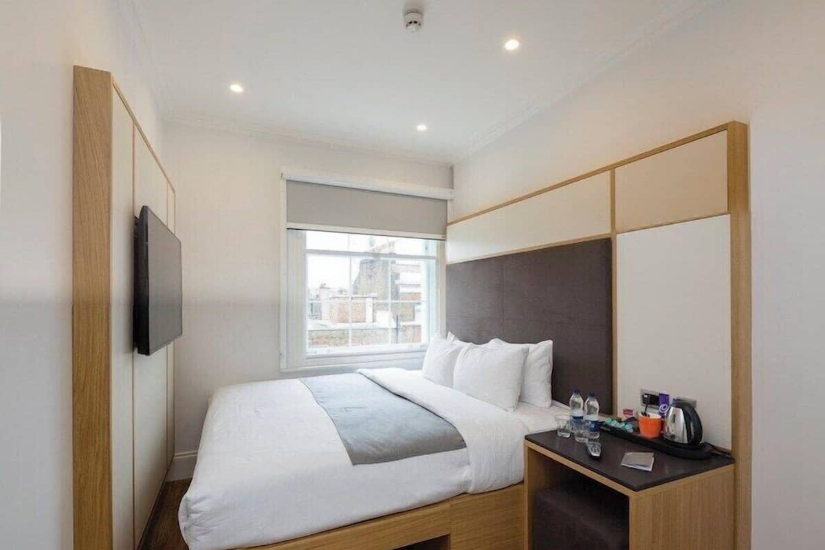 A modern hotel room with a bed, a desk, a TV, and a window.