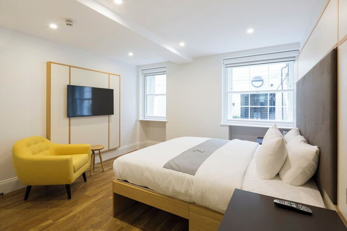 A modern bedroom with a bed, a TV mounted on the wall, and a yellow armchair.