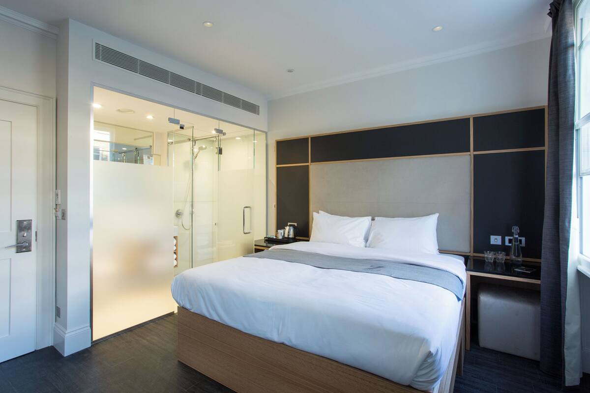 A modern hotel room with a large bed, a walk-in closet, and a bathroom with a glass shower enclosure.