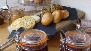 Variedad de productos horneados, como muffins, bagels y pasteles, sobre una tabla de madera, junto con botes de mermelada.