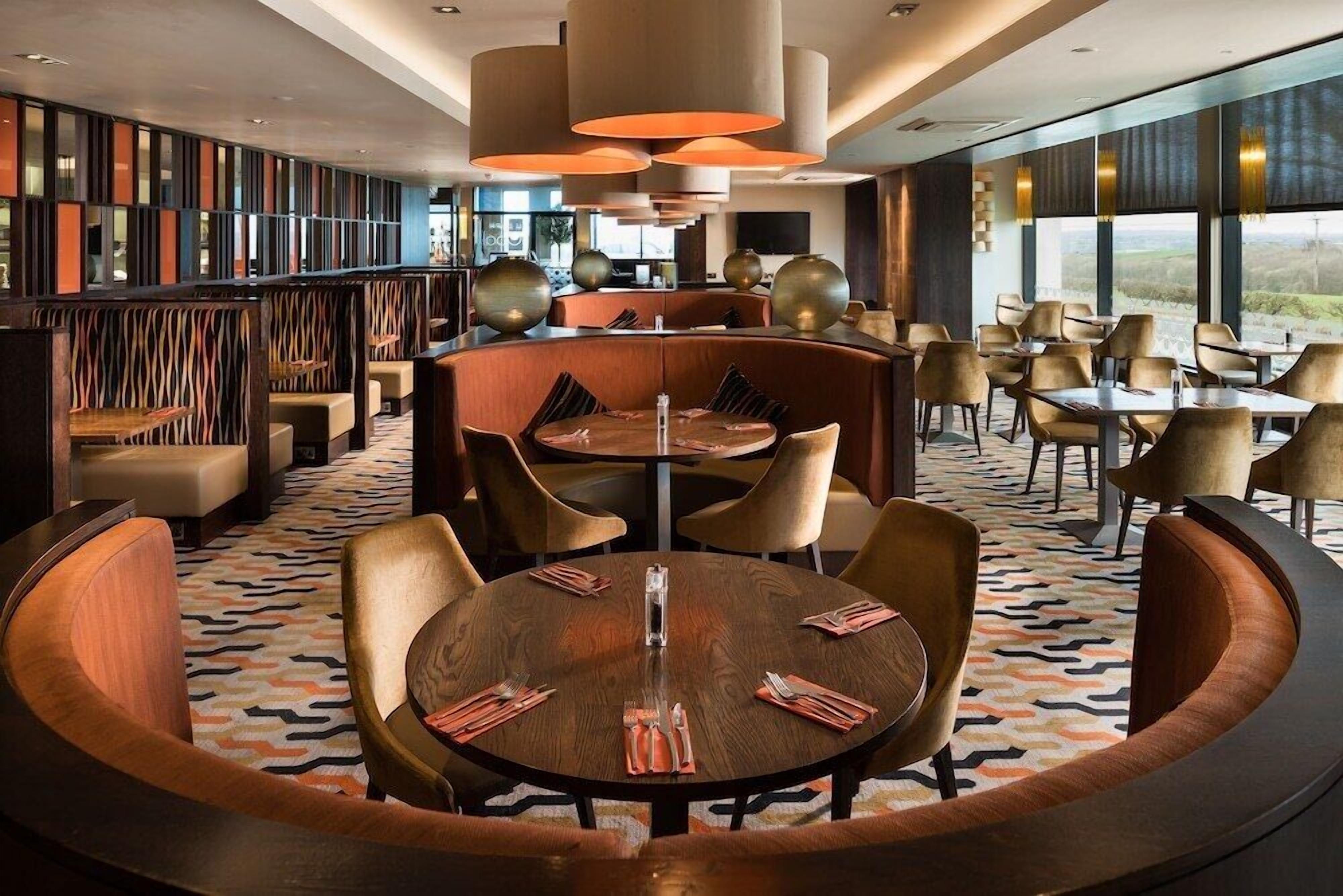A modern restaurant with round tables, cushioned seating, and large windows offering a view.