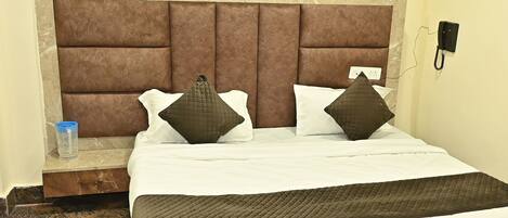 A hotel room with a large bed, two pillows, a bedside table, and a phone on the wall.