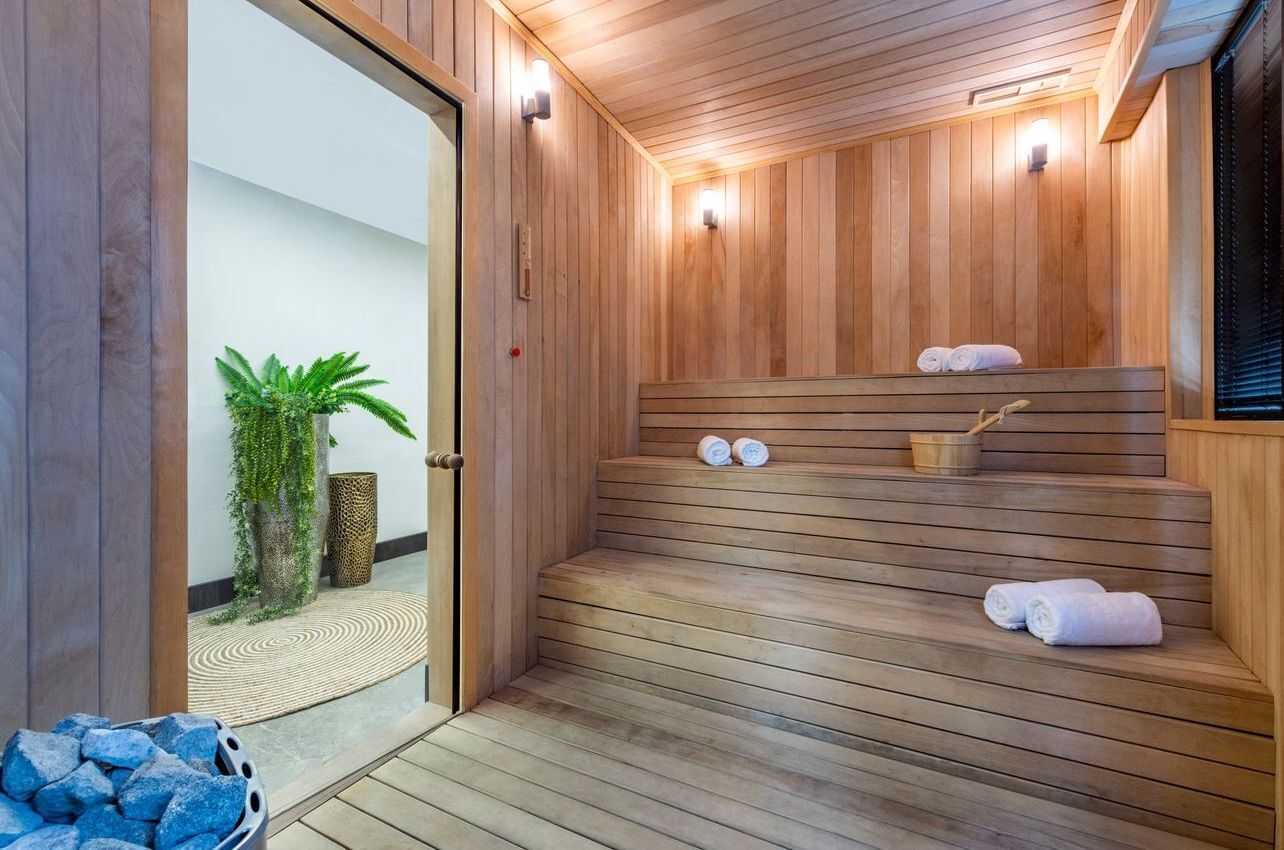 A wooden sauna with steps and a bench, a small plant, and a towel rack.