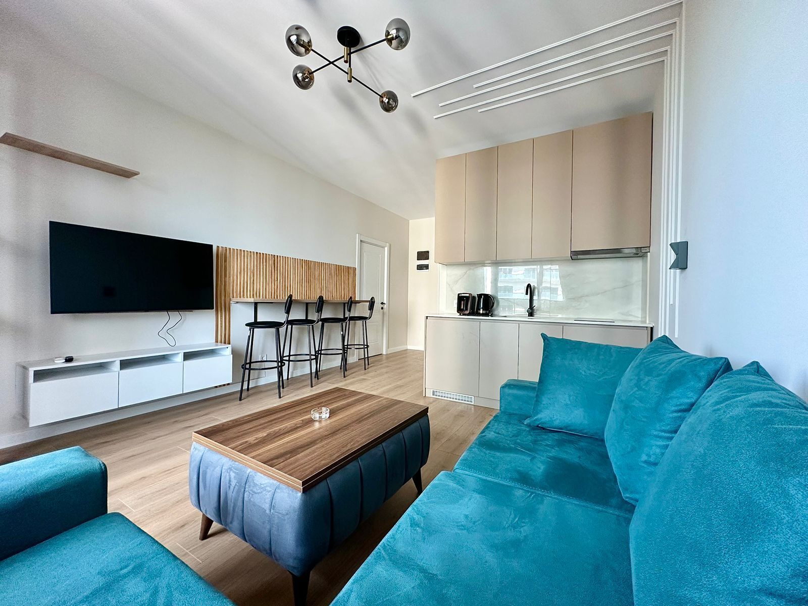 A modern living room with a wooden coffee table, teal sofas, and a TV mounted on the wall.
