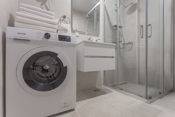 Un baño moderno con lavadora de carga frontal, ducha con cerramiento de vidrio y tocador blanco.