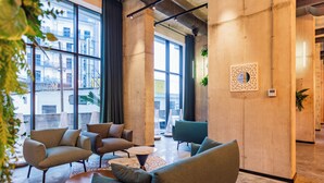 A modern lounge area with large windows, comfortable seating, and a decorative wall piece. - Nova Concierge (Batumi)