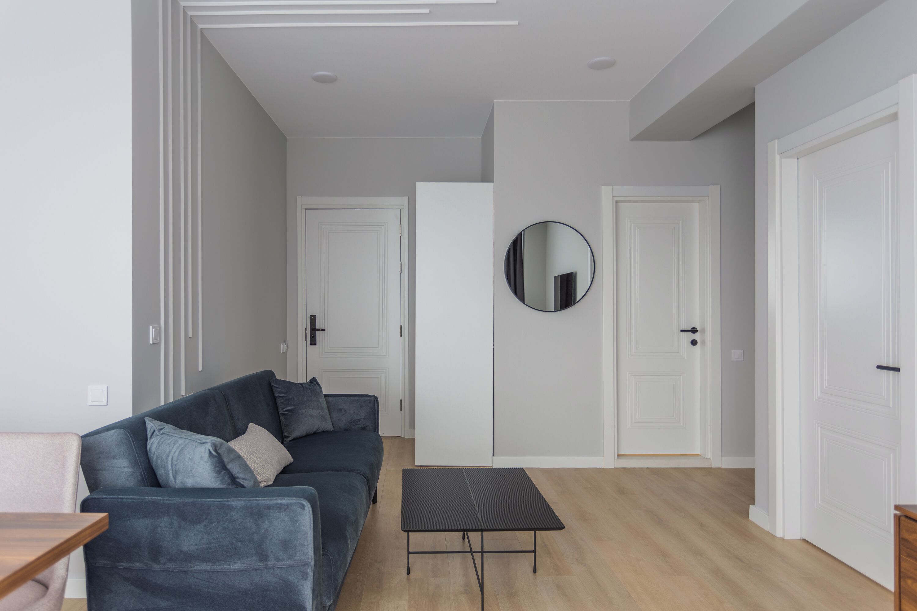 A modern living room with a dark grey sofa, a round mirror, and a black coffee table.