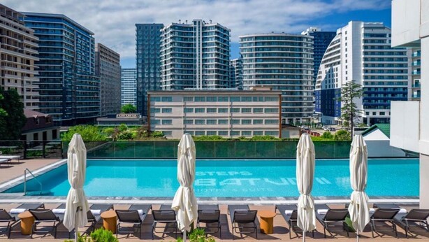 A rooftop pool with lounge chairs and umbrellas, surrounded by high-rise buildings. - Nova Concierge (Batumi)