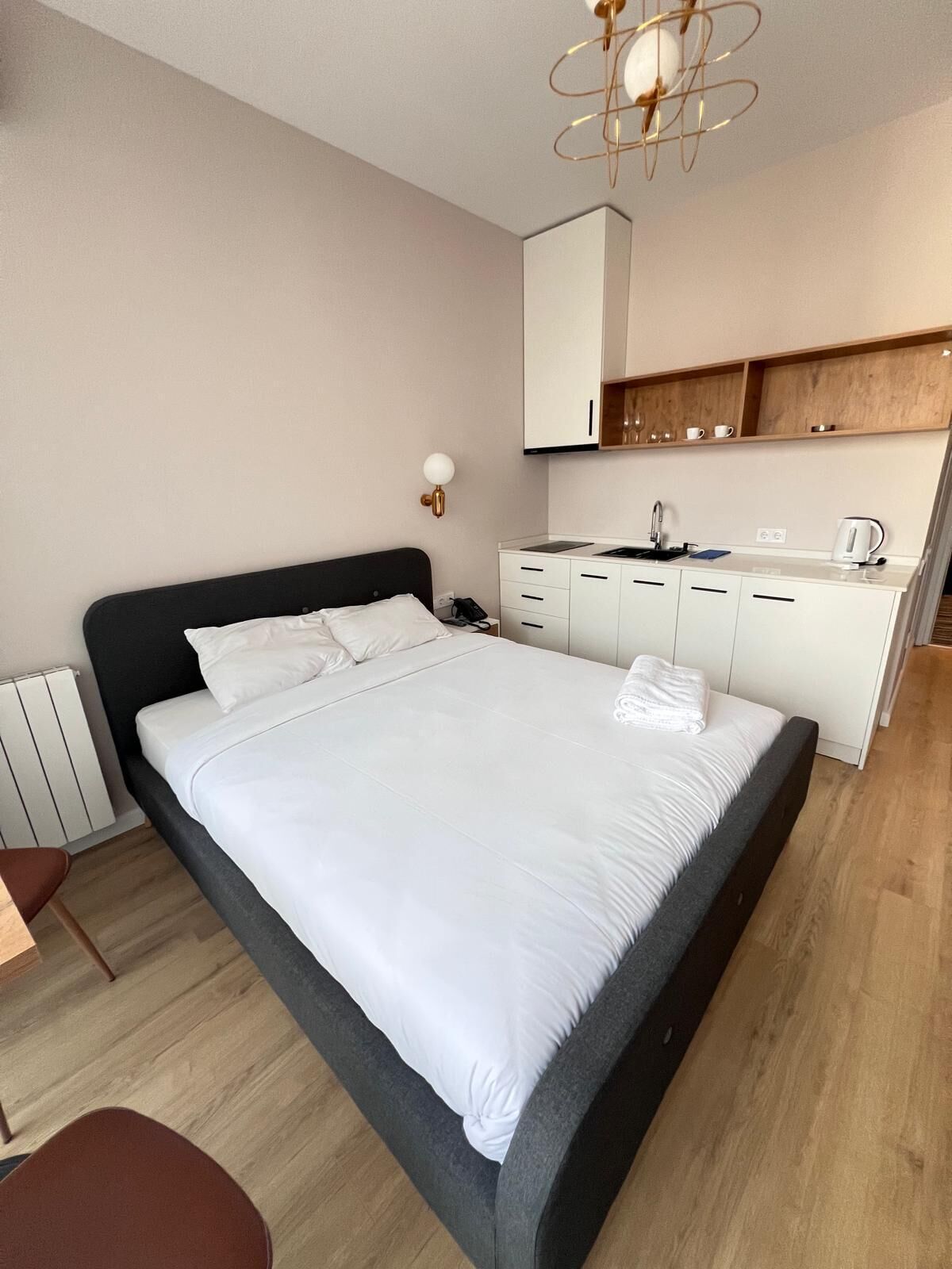 A modern hotel room with a large bed, a small kitchenette, and a wooden floor.