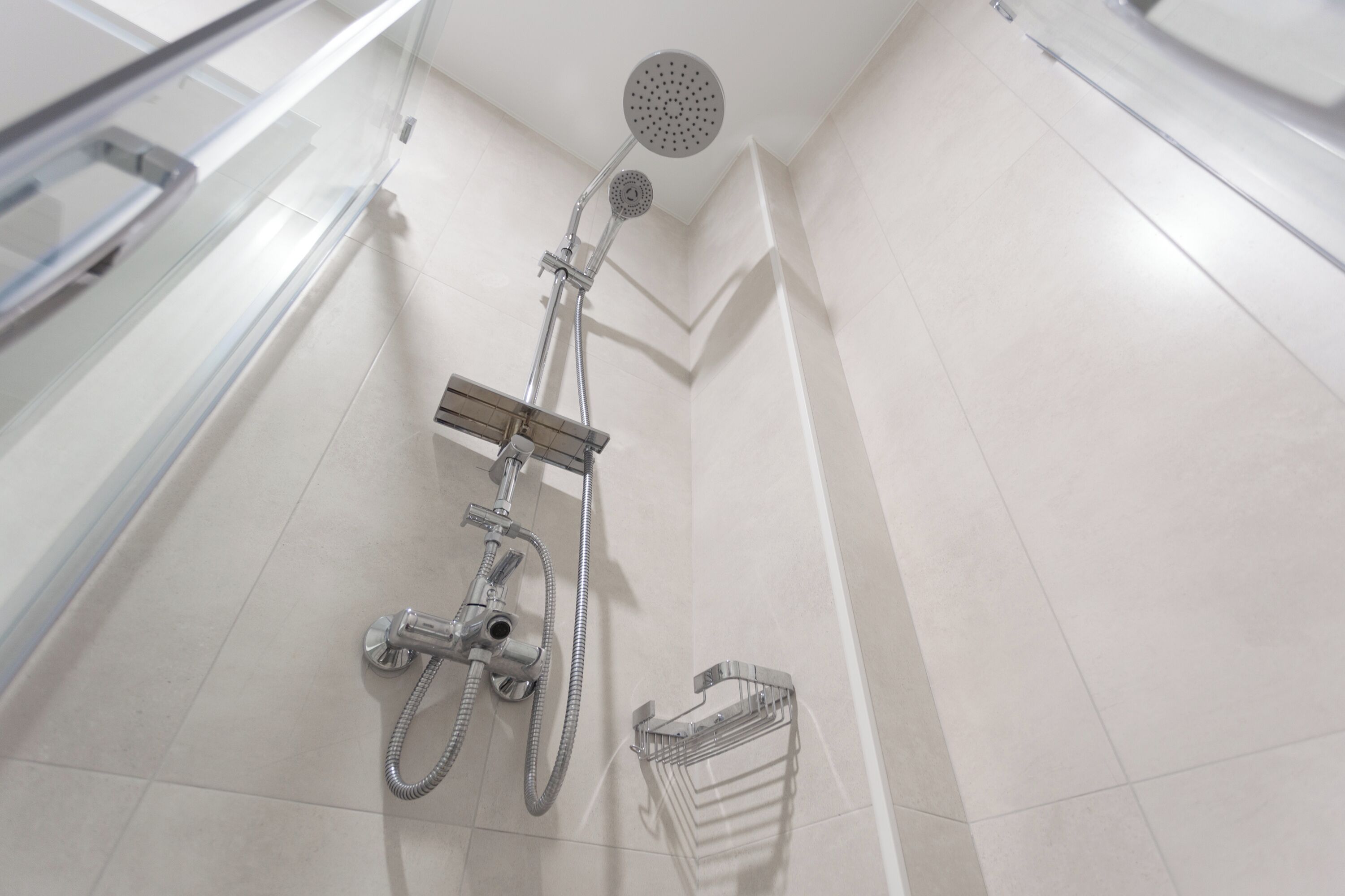 Une douche moderne dotée d’un pommeau de douche à main et d’un pommeau de douche fixe fixé au mur, d’un receveur de douche chromé et d’un porte-serviettes chromé.
