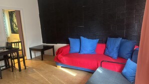 A room with a black brick wall, a red sofa with blue cushions, a small wooden table, and a chair. - Apartment Close to Stockholm City (Hägersten)