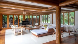 Un vaste espace de vie agrémenté de poutres en bois, de grandes fenêtres et d’un téléviseur à écran plat.
