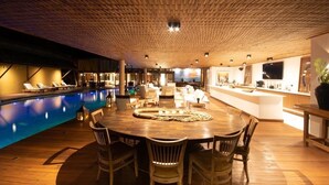 Un vaste espace intérieur doté d’une piscine, d’une table ronde en bois entourée de chaises et d’un coin bar avec des sièges.