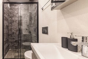 A modern bathroom with a glass-enclosed shower, a white sink, and a marble-tiled shower area.