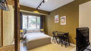 Quarto de hotel com uma cama, escrivaninha, cadeira, televisão e duas obras de arte emolduradas na parede.