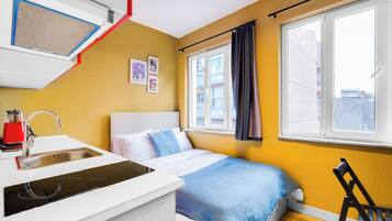 Quarto compacto com cama, pia e janela com cortinas.