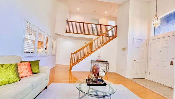 A spacious living room with a white sofa, a glass coffee table, and a wooden staircase.