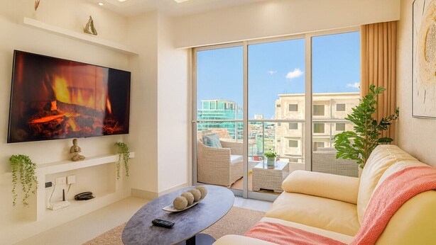 Ein modernes Wohnzimmer mit Flachbildfernseher, einer Couch, einem Couchtisch und einem Balkon mit Blick auf die Stadt.