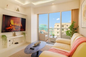 Ein modernes Wohnzimmer mit Flachbildfernseher, einer Couch, einem Couchtisch und einem Balkon mit Blick auf die Stadt.